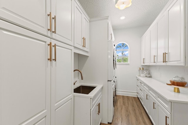 laundry room featuring cabinet space, stacked washer and clothes dryer, light wood-style floors, and baseboards
