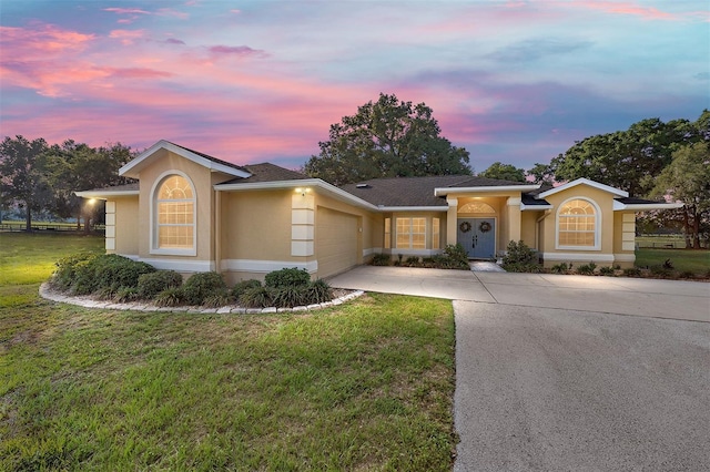 ranch-style house with a garage, stucco siding, driveway, and a lawn