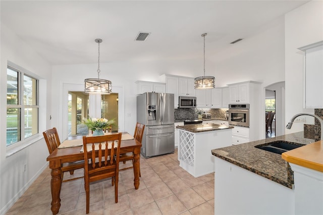 kitchen featuring appliances with stainless steel finishes, a sink, decorative backsplash, a kitchen island, and a chandelier