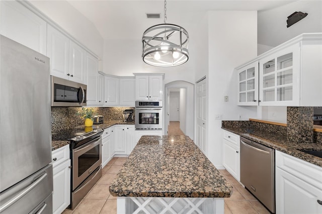 kitchen with stainless steel appliances, light tile patterned flooring, decorative backsplash, arched walkways, and a towering ceiling