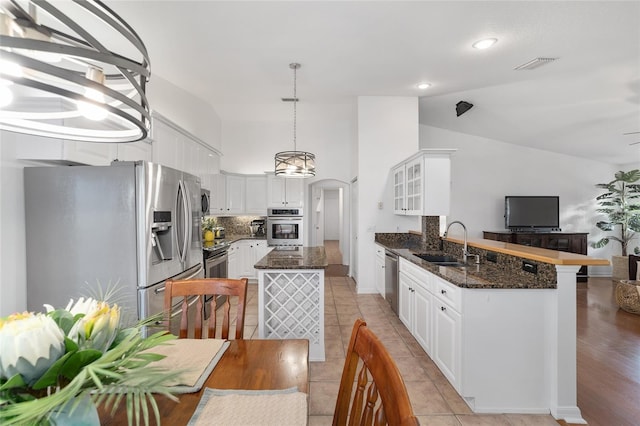 kitchen with appliances with stainless steel finishes, a sink, a peninsula, lofted ceiling, and white cabinetry