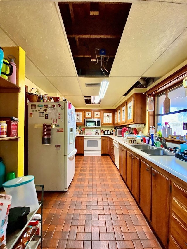 kitchen with white appliances, a sink, light countertops, brick patterned floors, and brown cabinetry