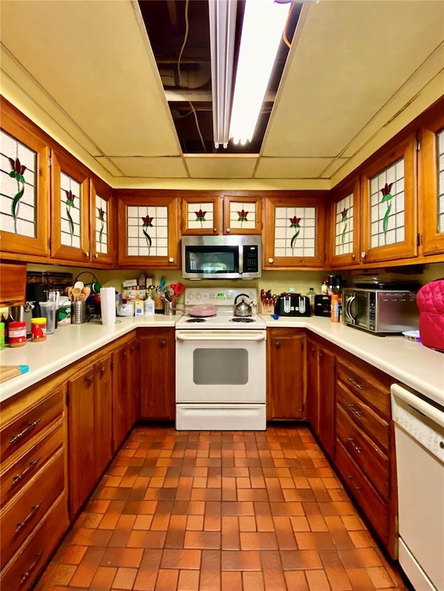 kitchen featuring white appliances, light countertops, glass insert cabinets, and brown cabinets