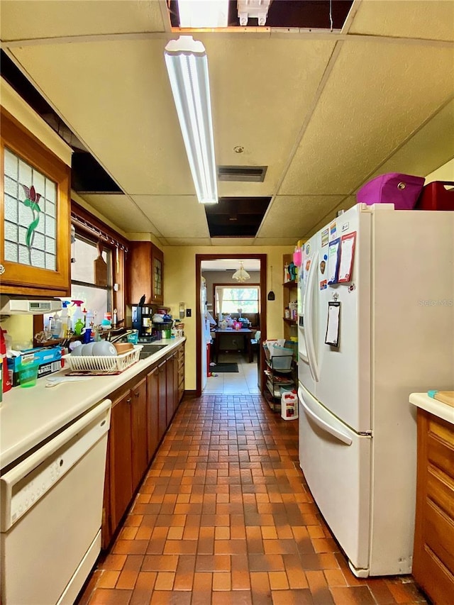 kitchen featuring white appliances, brown cabinetry, light countertops, and a paneled ceiling