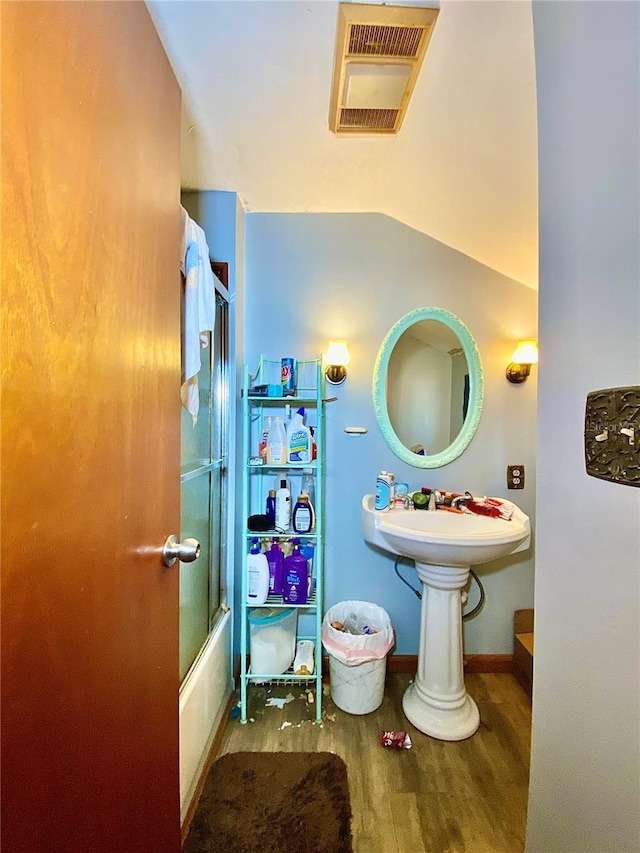 bathroom featuring wood finished floors, combined bath / shower with glass door, and a sink