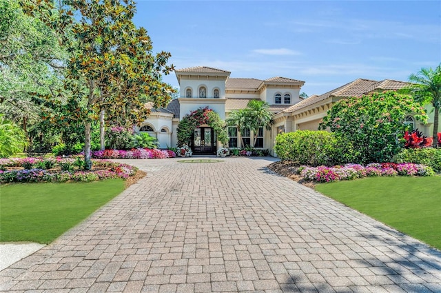 mediterranean / spanish-style house with curved driveway, stucco siding, an attached garage, and a front lawn