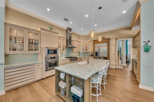 kitchen with built in appliances, wall chimney range hood, a sink, a breakfast bar, and an island with sink