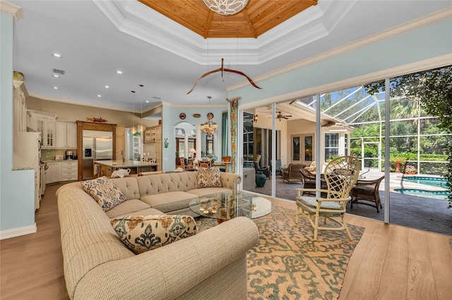 living room featuring ornamental molding, light wood finished floors, a sunroom, recessed lighting, and a tray ceiling