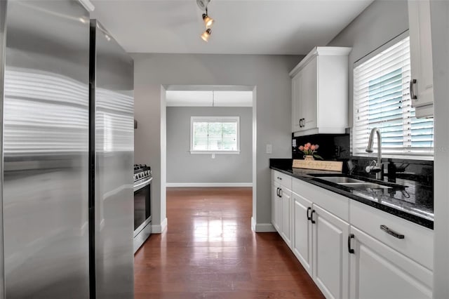 kitchen with appliances with stainless steel finishes, a sink, white cabinetry, dark wood-type flooring, and baseboards