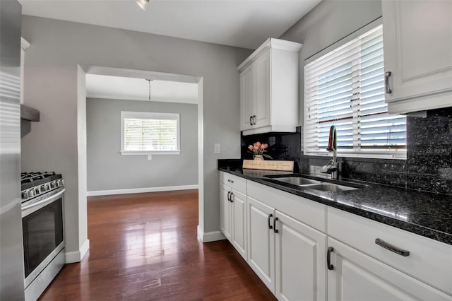 kitchen featuring gas range, a sink, backsplash, baseboards, and dark wood finished floors