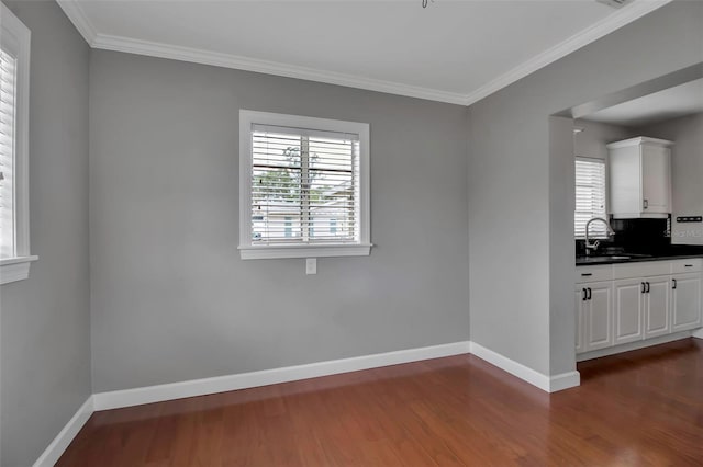 unfurnished dining area featuring a sink, dark wood-style floors, baseboards, and crown molding