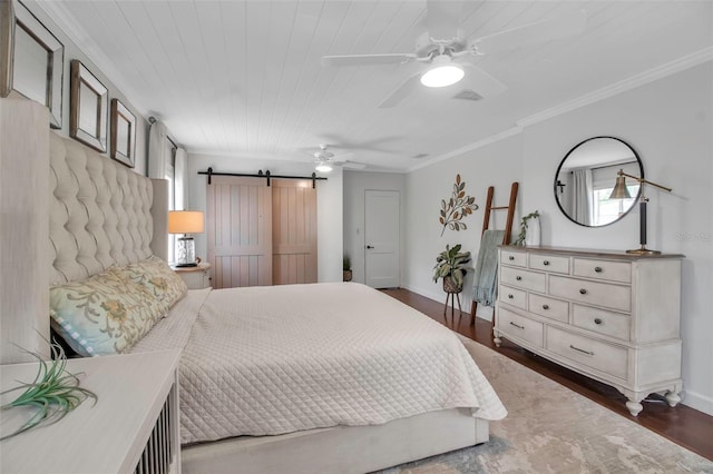 bedroom with baseboards, wood finished floors, a barn door, and ornamental molding