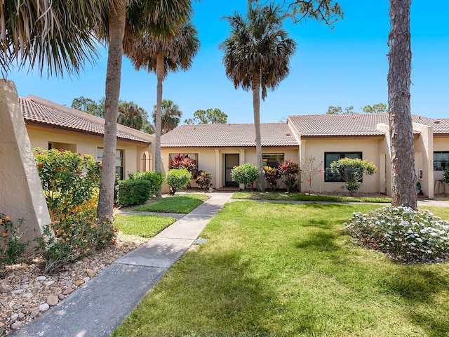 view of front facade featuring a tiled roof, a front lawn, and stucco siding