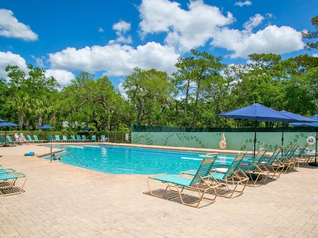 community pool with fence, a patio area, and view of wooded area