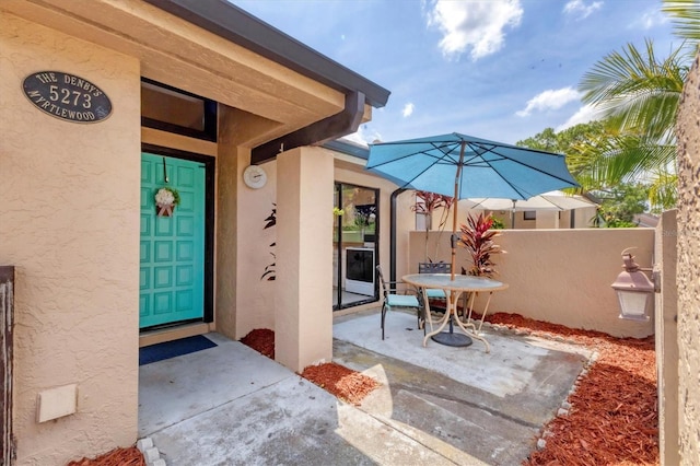 view of exterior entry featuring stucco siding, fence, and a patio area