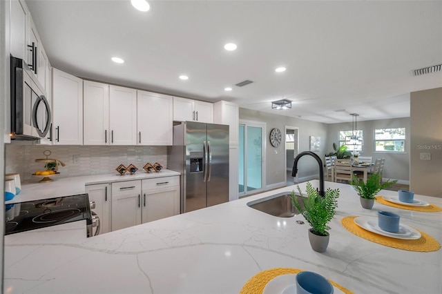 kitchen featuring appliances with stainless steel finishes, a sink, decorative backsplash, light stone countertops, and recessed lighting