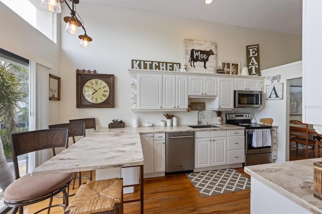 kitchen with stainless steel appliances, high vaulted ceiling, a sink, white cabinetry, and decorative backsplash