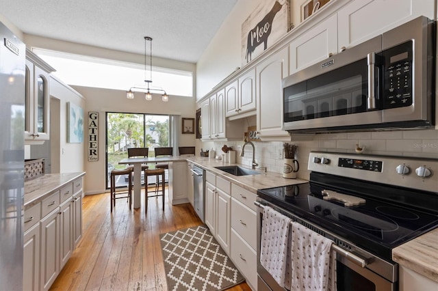 kitchen featuring appliances with stainless steel finishes, a sink, backsplash, light wood-style floors, and white cabinets