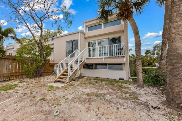 back of house with fence, stucco siding, and stairway