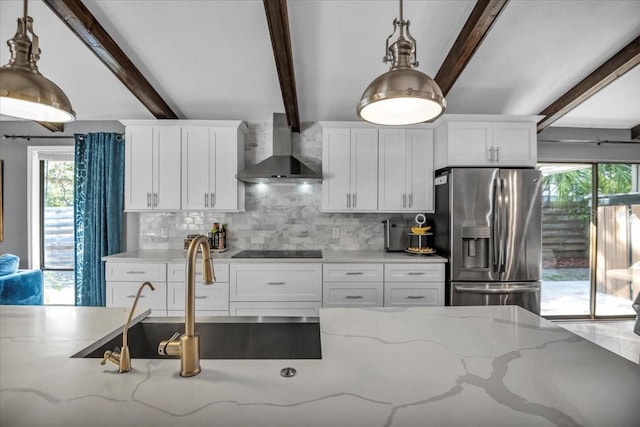 kitchen featuring stainless steel refrigerator with ice dispenser, wall chimney range hood, black electric cooktop, a sink, and white cabinetry