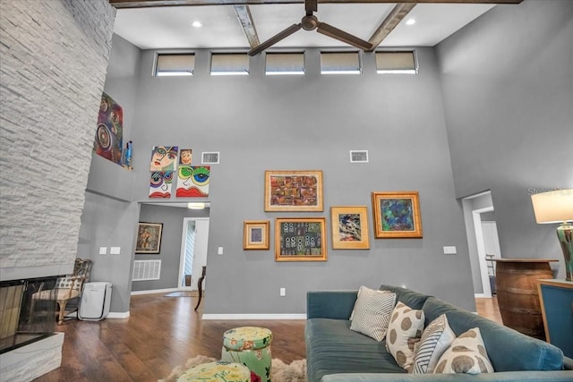 living room featuring a high ceiling, plenty of natural light, wood finished floors, a stone fireplace, and baseboards