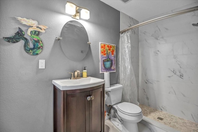 bathroom with tiled shower, vanity, toilet, and a textured wall