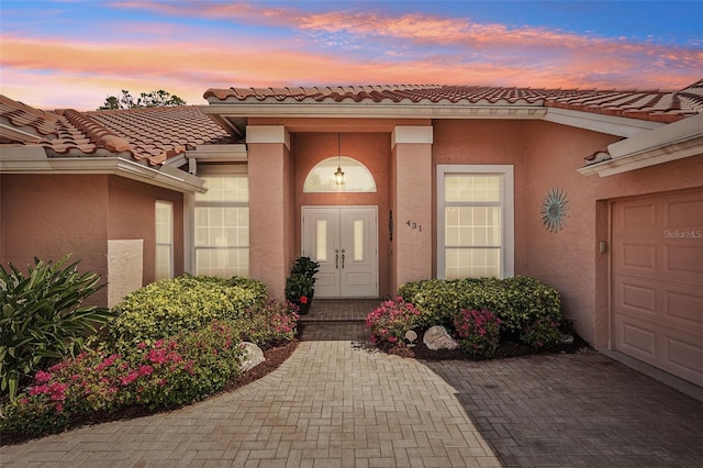431 Fieldstone Dr, Venice, FL 34292 - exterior entry at dusk featuring stucco siding, a garage, a tiled roof, and decorative driveway