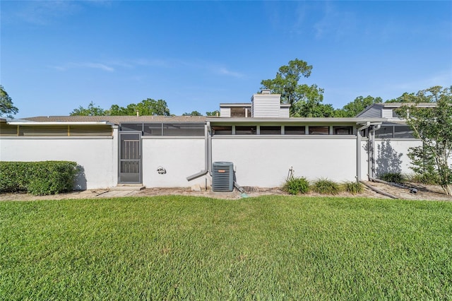 back of property with cooling unit, a lawn, and a chimney
