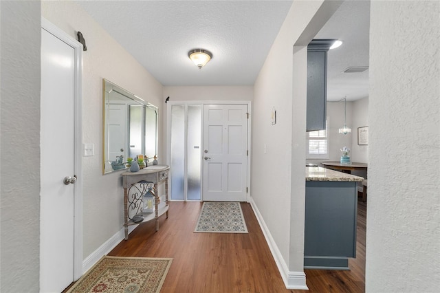 entryway featuring wood finished floors, a textured ceiling, baseboards, and a textured wall