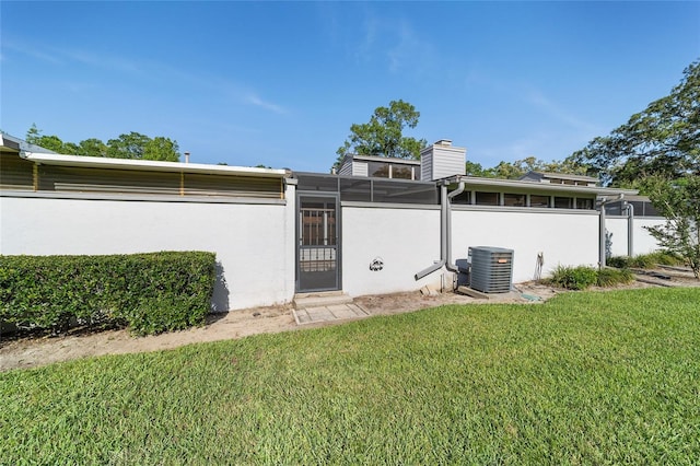 back of property with stucco siding, a chimney, central air condition unit, and a lawn