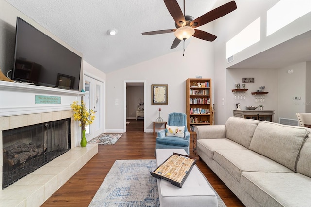 living area featuring ceiling fan, a tile fireplace, high vaulted ceiling, wood finished floors, and baseboards
