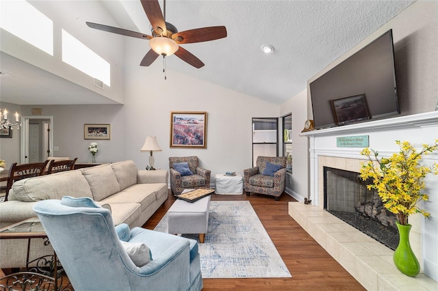 living area featuring a tiled fireplace, a ceiling fan, a chandelier, wood finished floors, and a textured ceiling