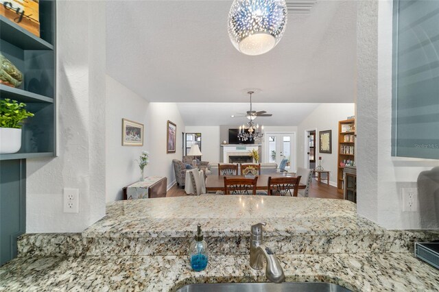 kitchen featuring a fireplace, a sink, wood finished floors, light stone countertops, and lofted ceiling