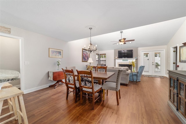 dining space featuring light wood-type flooring, a ceiling fan, baseboards, and a tile fireplace