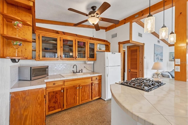 kitchen with a sink, stainless steel microwave, freestanding refrigerator, black stovetop, and beam ceiling