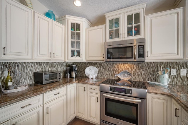 229 S Harbor Dr, Holmes Beach, FL 34217 - kitchen with stainless steel appliances, backsplash, glass insert cabinets, a textured ceiling, and dark stone countertops