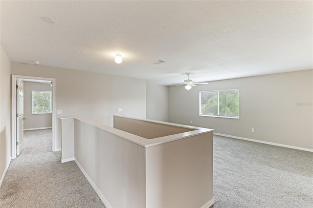 hallway featuring light carpet, an upstairs landing, a textured ceiling, and baseboards