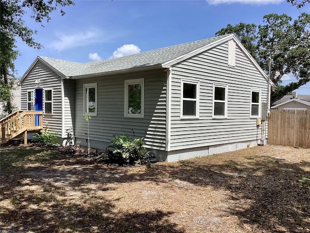 back of house featuring fence, a shingled roof, and crawl space