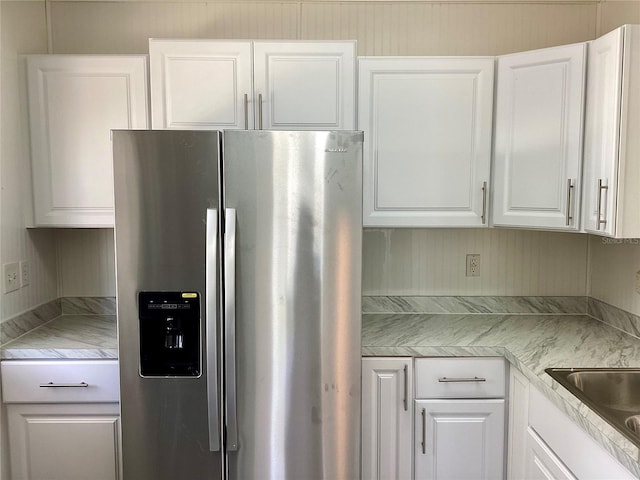 kitchen featuring stainless steel fridge, white cabinets, and light countertops