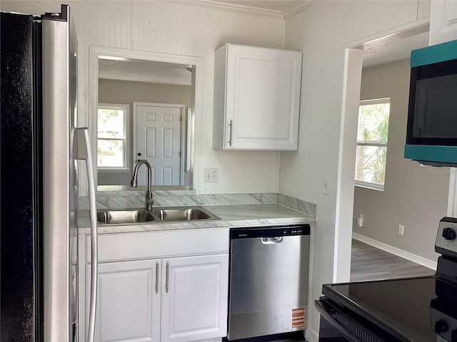 kitchen with stainless steel appliances, a sink, white cabinets, light countertops, and ornamental molding