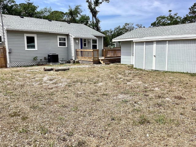 back of house featuring a wooden deck, an outdoor structure, roof with shingles, and central air condition unit