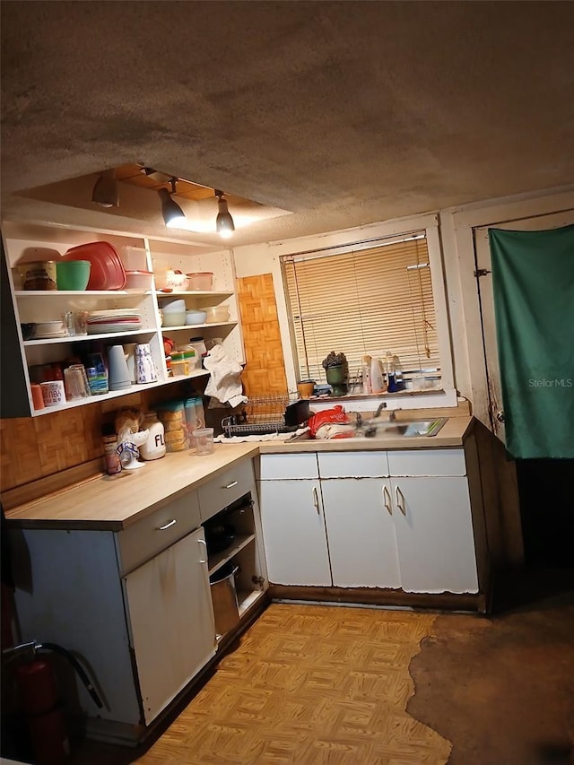 kitchen featuring a sink, white cabinets, a textured ceiling, open shelves, and light countertops