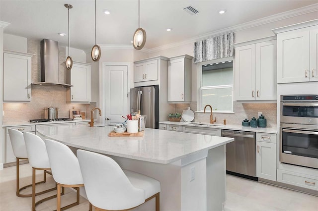 kitchen with appliances with stainless steel finishes, a sink, wall chimney range hood, a breakfast bar, and a kitchen island with sink