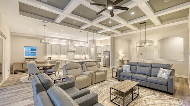 living room featuring a towering ceiling, light wood-type flooring, baseboards, beam ceiling, and ceiling fan