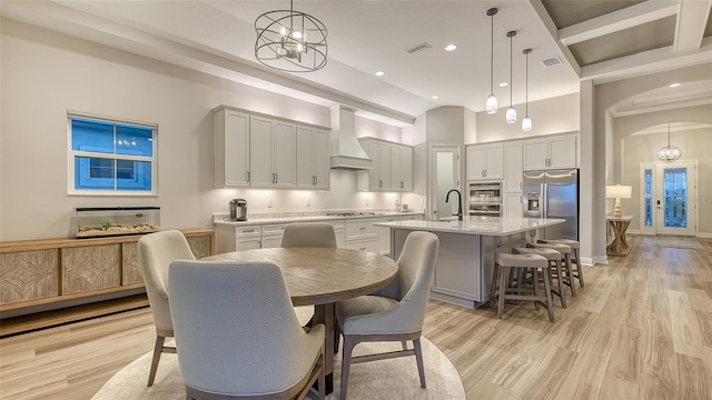 kitchen featuring custom exhaust hood, stainless steel refrigerator with ice dispenser, an island with sink, light countertops, and pendant lighting