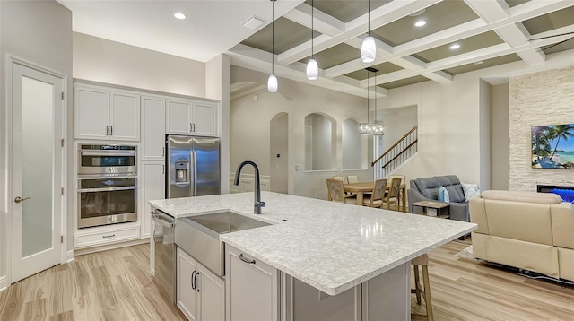 kitchen with stainless steel appliances, a sink, open floor plan, beamed ceiling, and light wood-style floors