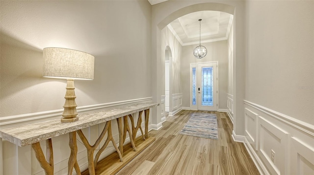 foyer with arched walkways, ornamental molding, a decorative wall, light wood-style floors, and wainscoting