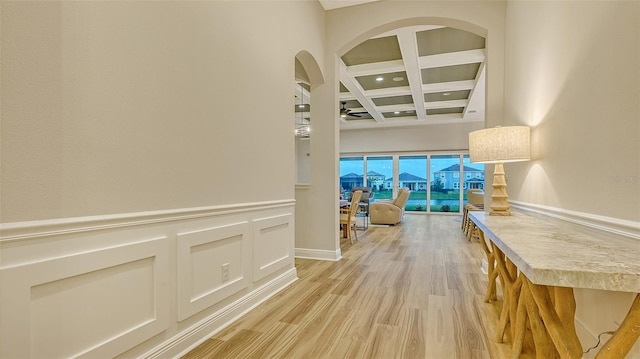 hallway featuring coffered ceiling, beamed ceiling, light wood-type flooring, arched walkways, and a towering ceiling