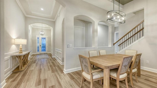 dining room featuring arched walkways, light wood-style flooring, ornamental molding, a chandelier, and a decorative wall