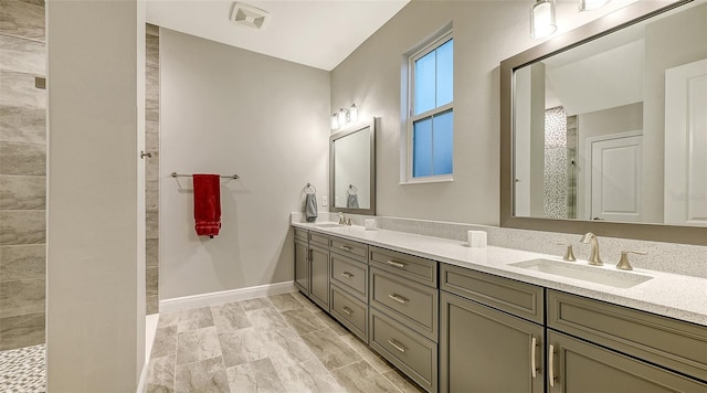 bathroom featuring tiled shower, double vanity, and baseboards
